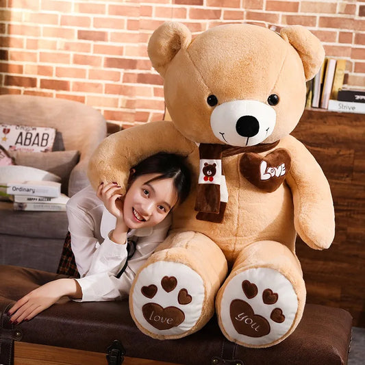 Person sitting behind a large teddy bear with 'love' and 'you' on paws, in a cozy room.