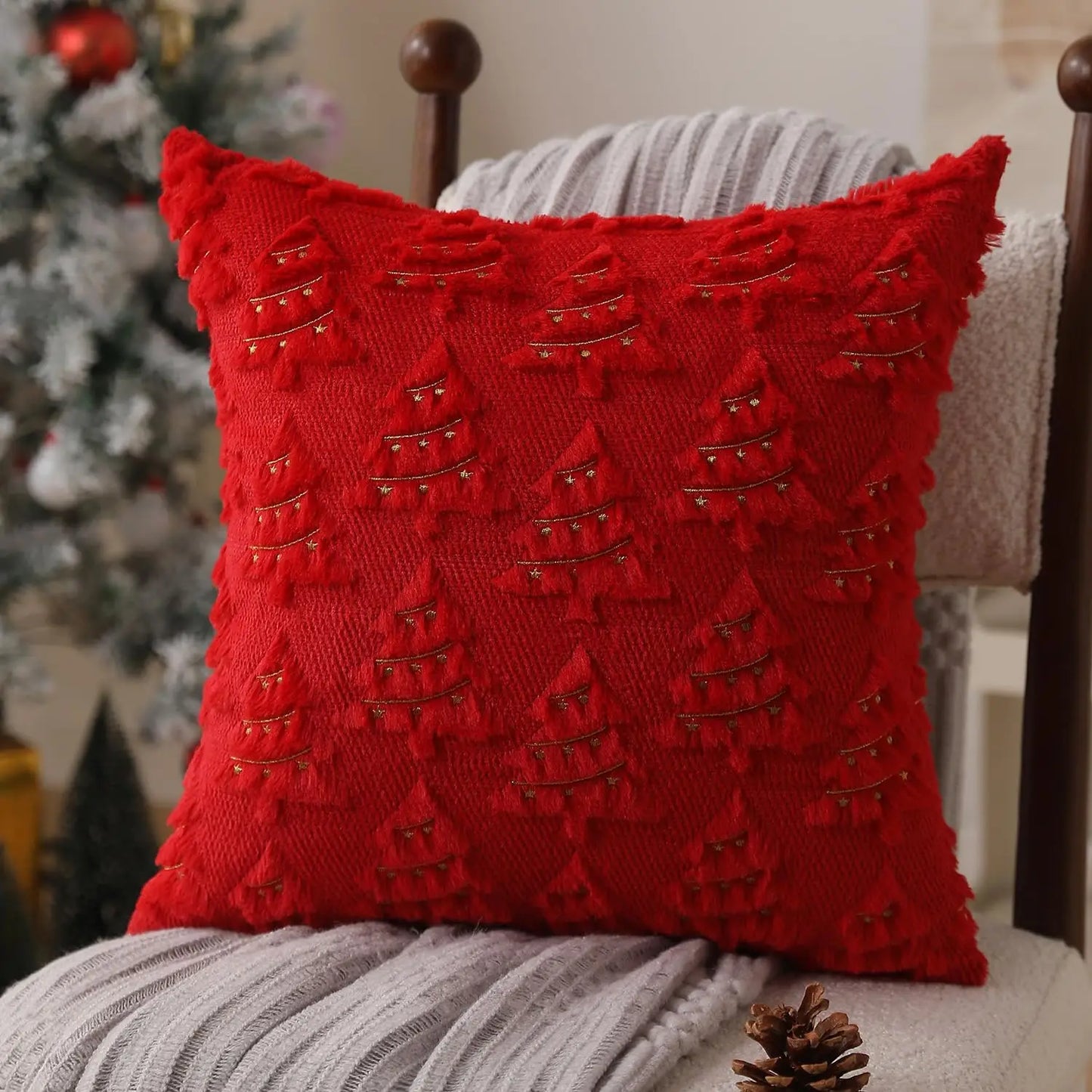 Red textured pillow with Christmas tree pattern on a chair with a blurred Christmas tree in the background.