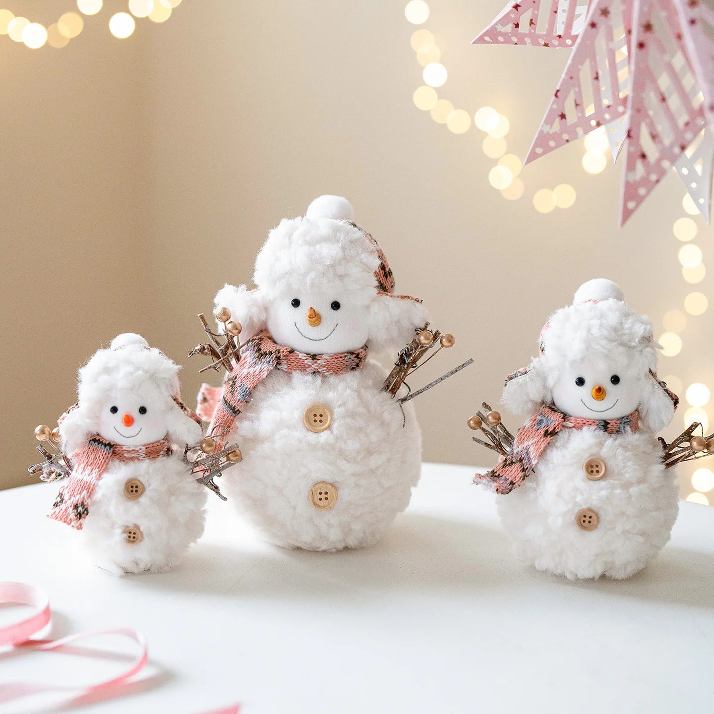 Three white snowman decorations with buttons and scarves on a blurred festive background.