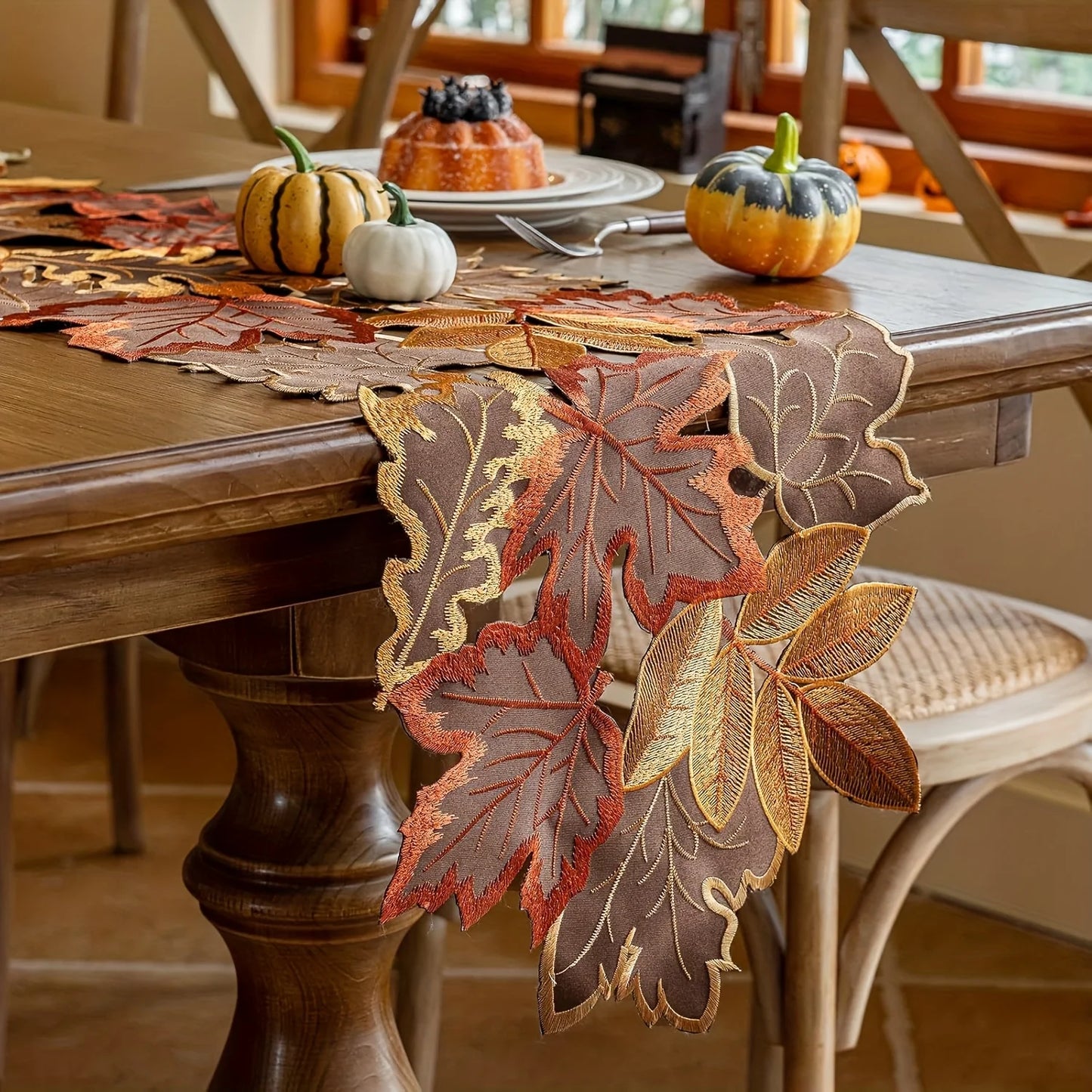 Decorative leaf-patterned table runner on a wooden table with pumpkins and fall-themed decor.