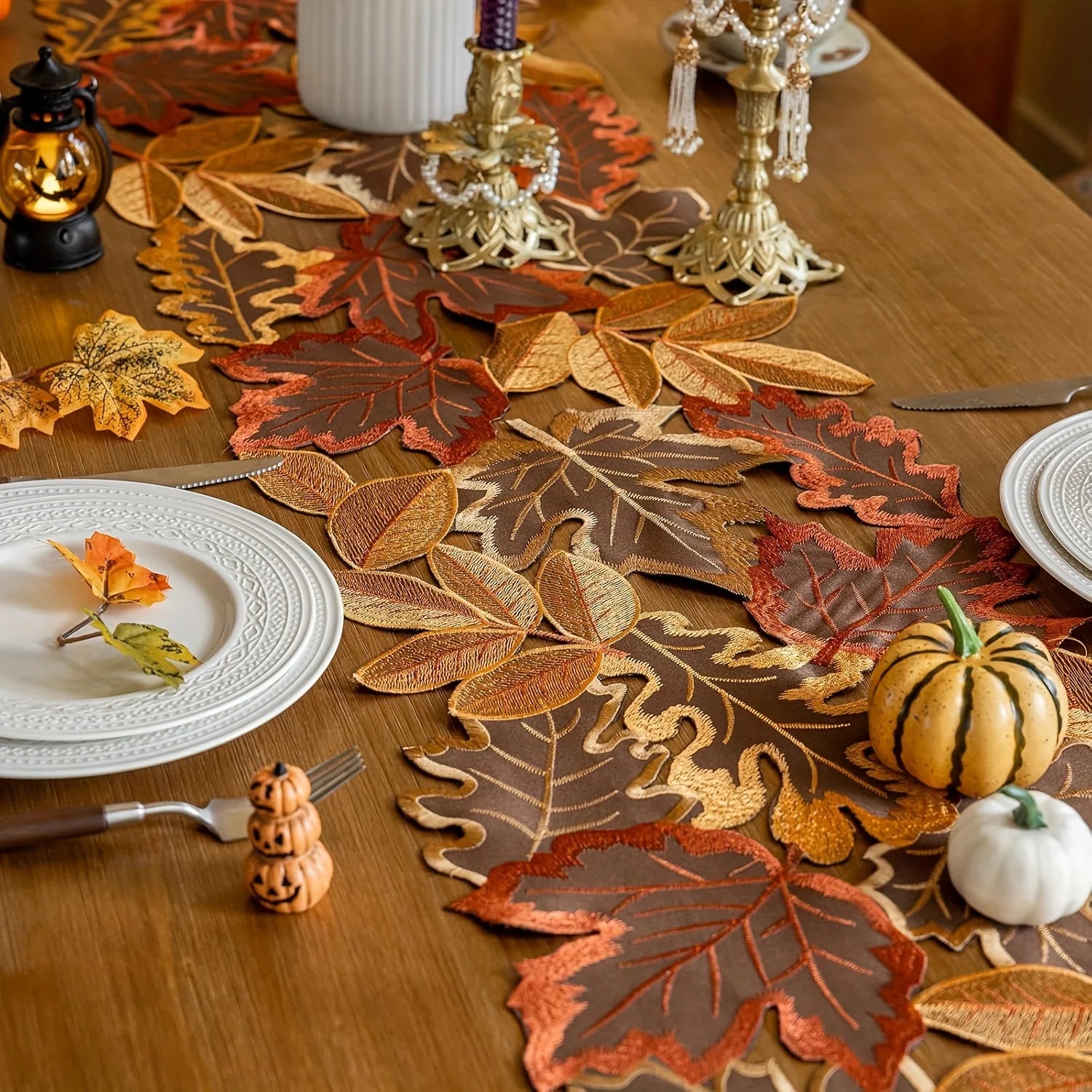 Decorative table setting with leaf-patterned placemats and small pumpkins on a wooden table.
