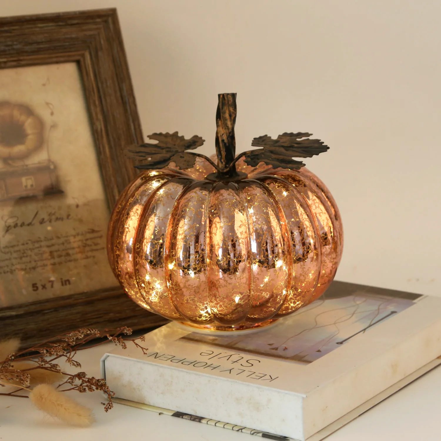 Decorative glass pumpkin on a surface with books and a framed picture in the background