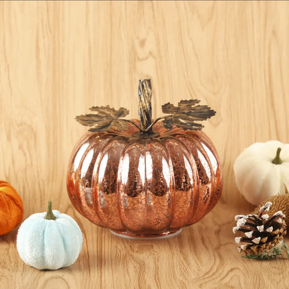 Decorative copper pumpkin on a wooden surface with other pumpkins and a pine cone.