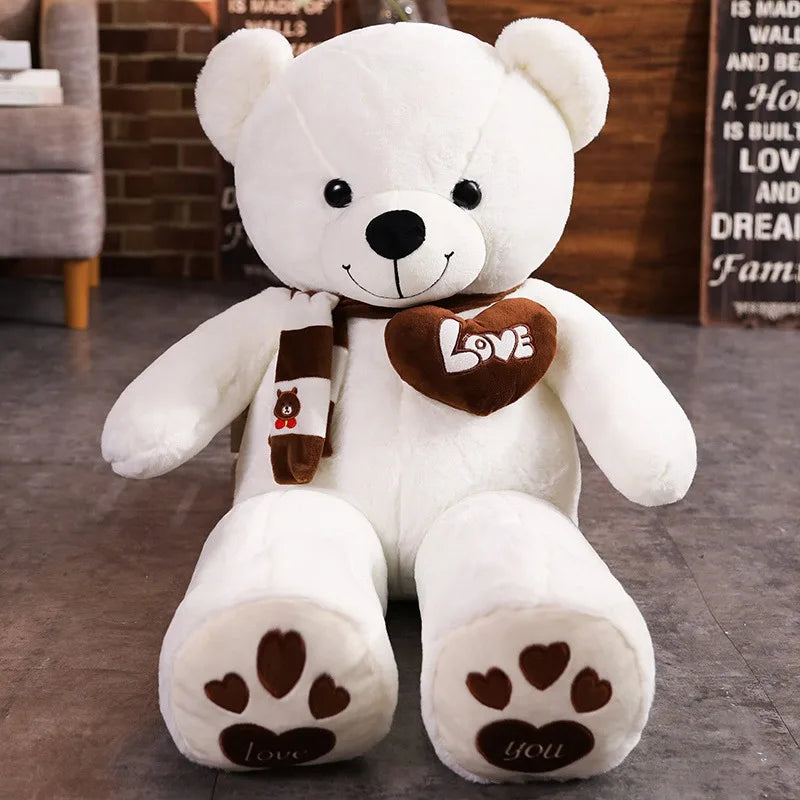 White teddy bear with a brown 'LOVE' heart and scarf on a wooden floor.
