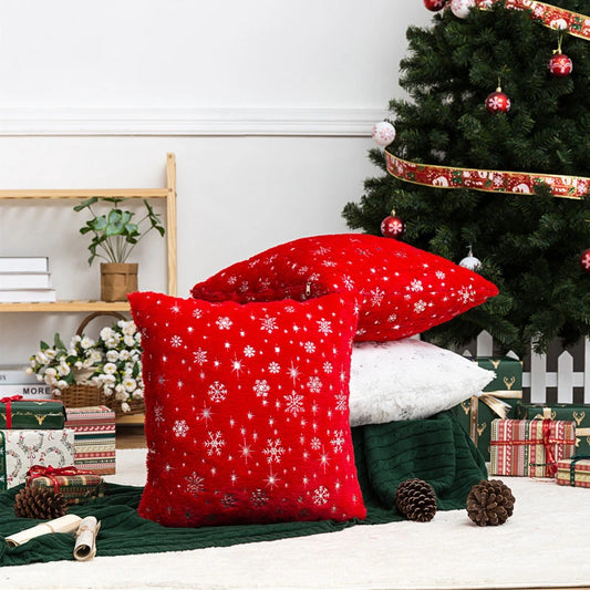 Red decorative pillows with snowflake patterns on a couch next to a Christmas tree.