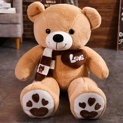 Plush teddy bear with a scarf and heart-shaped 'Love' pillow on a wooden floor.