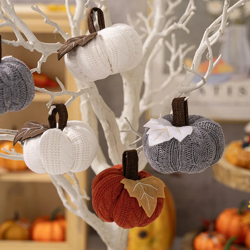 Decorative pumpkins made of knit material hanging on a white branch tree with blurred background.