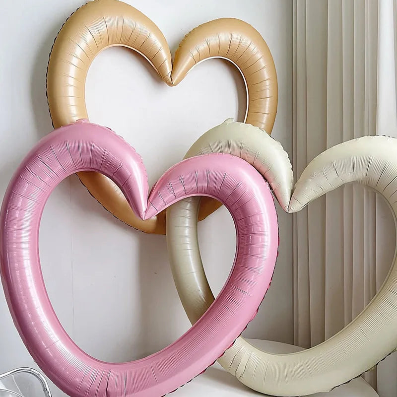 Three heart-shaped balloons in gold, pink, and beige against a white wall.