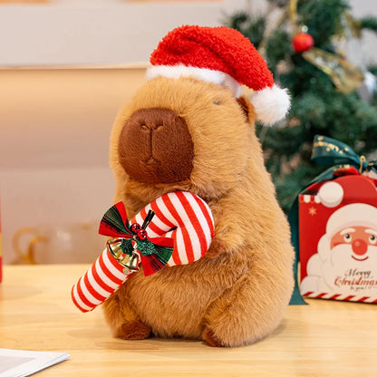 Plush capybara wearing a Santa hat and holding a candy cane with a Christmas tree in the background