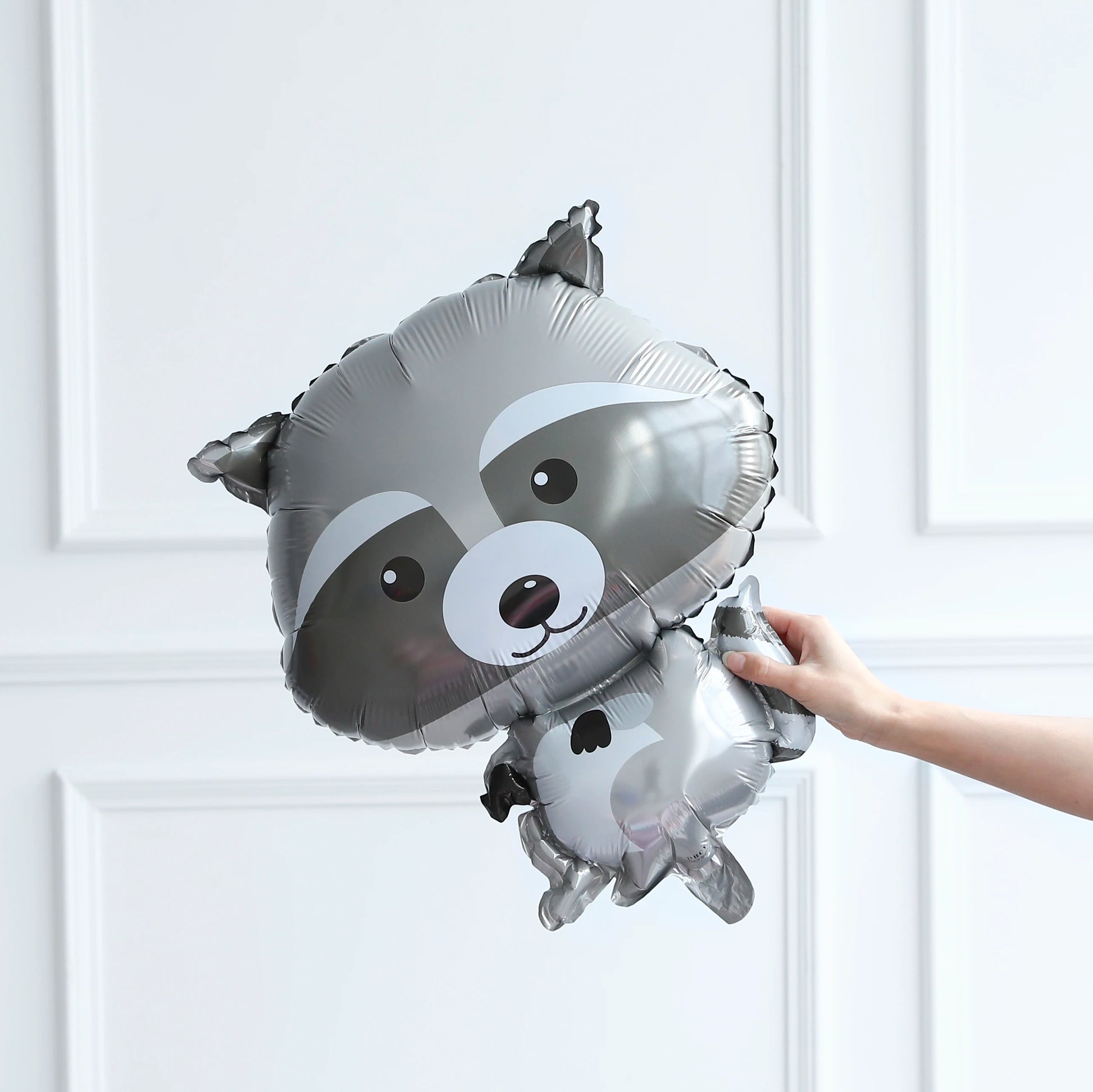 Raccoon-shaped balloon held by a hand against a white background