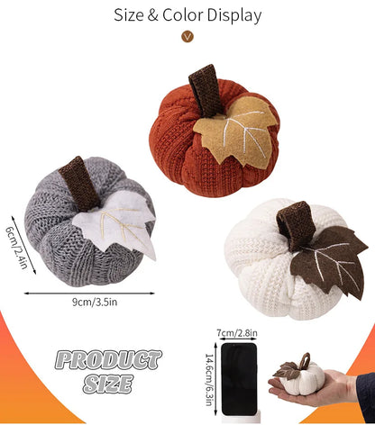 Three knitted pumpkins in different colors with leaf decorations, shown with measurements and a smartphone for scale.