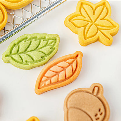 Colorful leaf-shaped cookies on a white surface with a cooling rack in the background.