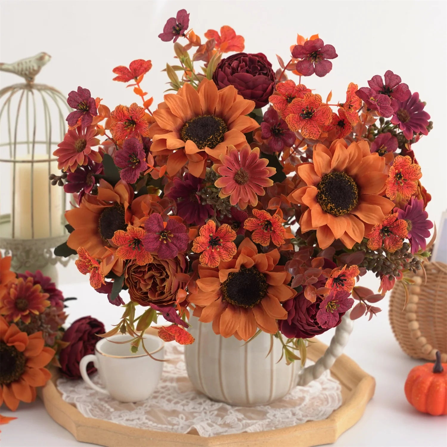 Autumn-themed floral arrangement with orange, red, and purple flowers in a white vase on a lace-tray.