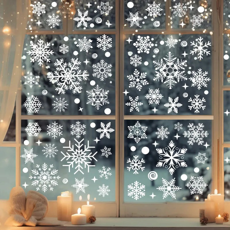Decorative window stickers with snowflakes on a glass pane, with candles and decorative items on a table below.