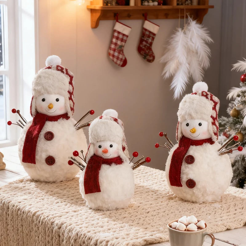 Three snowman decorations with scarves on a surface near a Christmas tree and stockings.