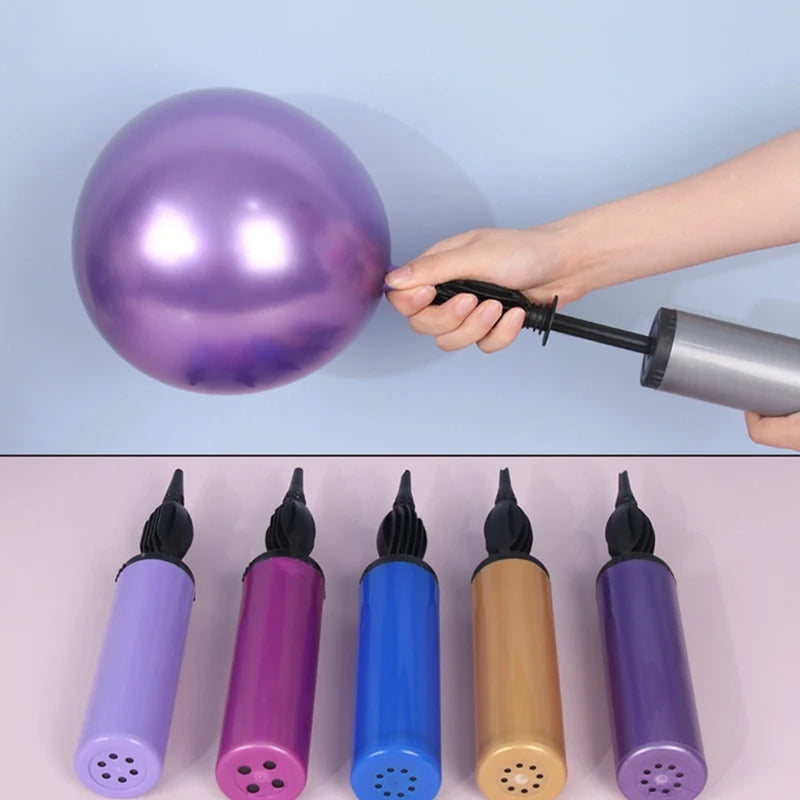 Hand using a balloon pump to inflate a purple balloon with five other colorful balloon pumps on a pink background.