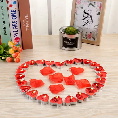 Heart-shaped arrangement of red candles and flower petals on a wooden surface with books and a plant pot in the background.