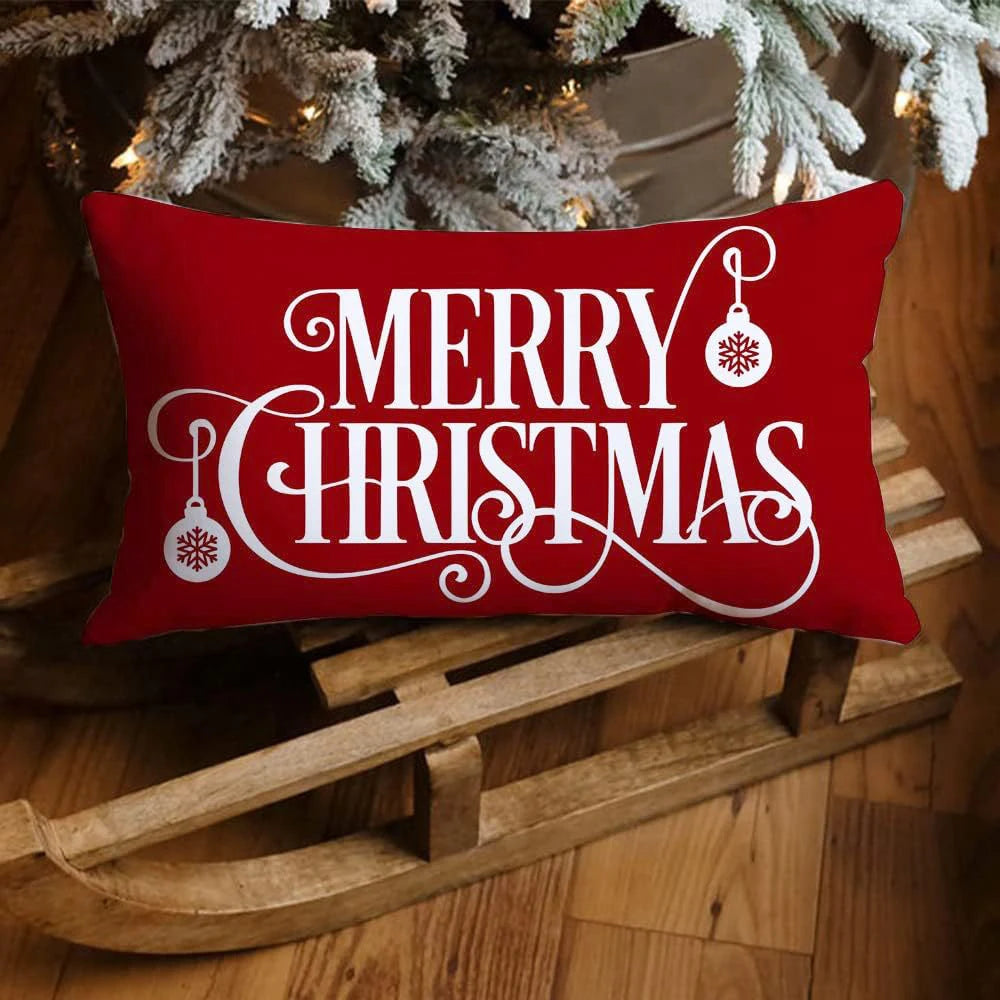 Red pillow with 'Merry Christmas' text in front of a decorated Christmas tree.