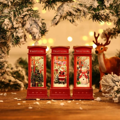 Three red telephone booths with Christmas scenes inside, surrounded by festive decorations including a reindeer and snow-covered trees.