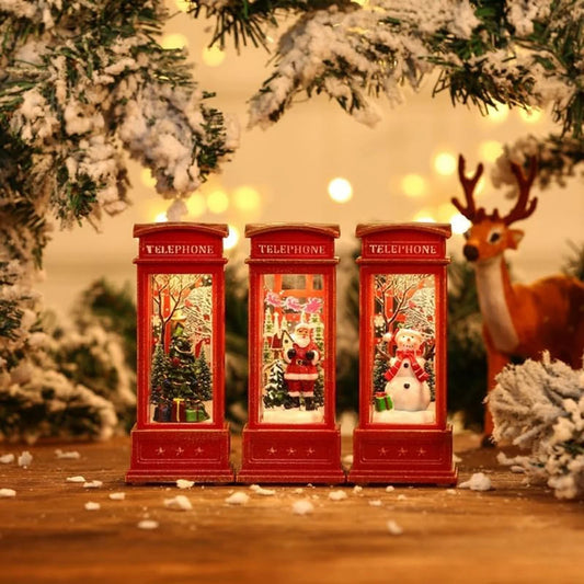 Three red telephone booths with Christmas scenes inside, surrounded by festive decorations including a reindeer and snow-covered trees.