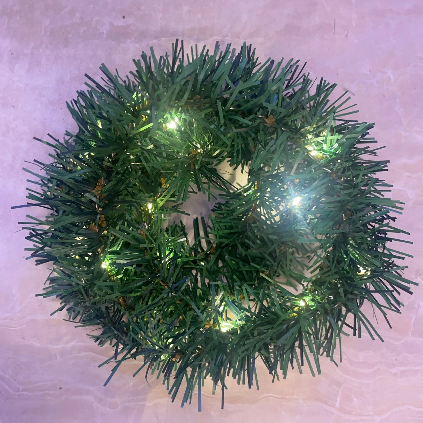 Green Christmas wreath with lights on a light pink background