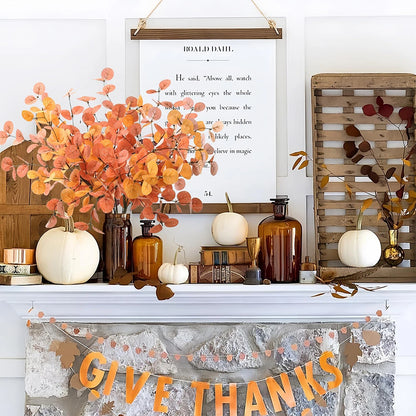 Decorative autumn mantel with pumpkins, leaves, and 'Give Thanks' banner.