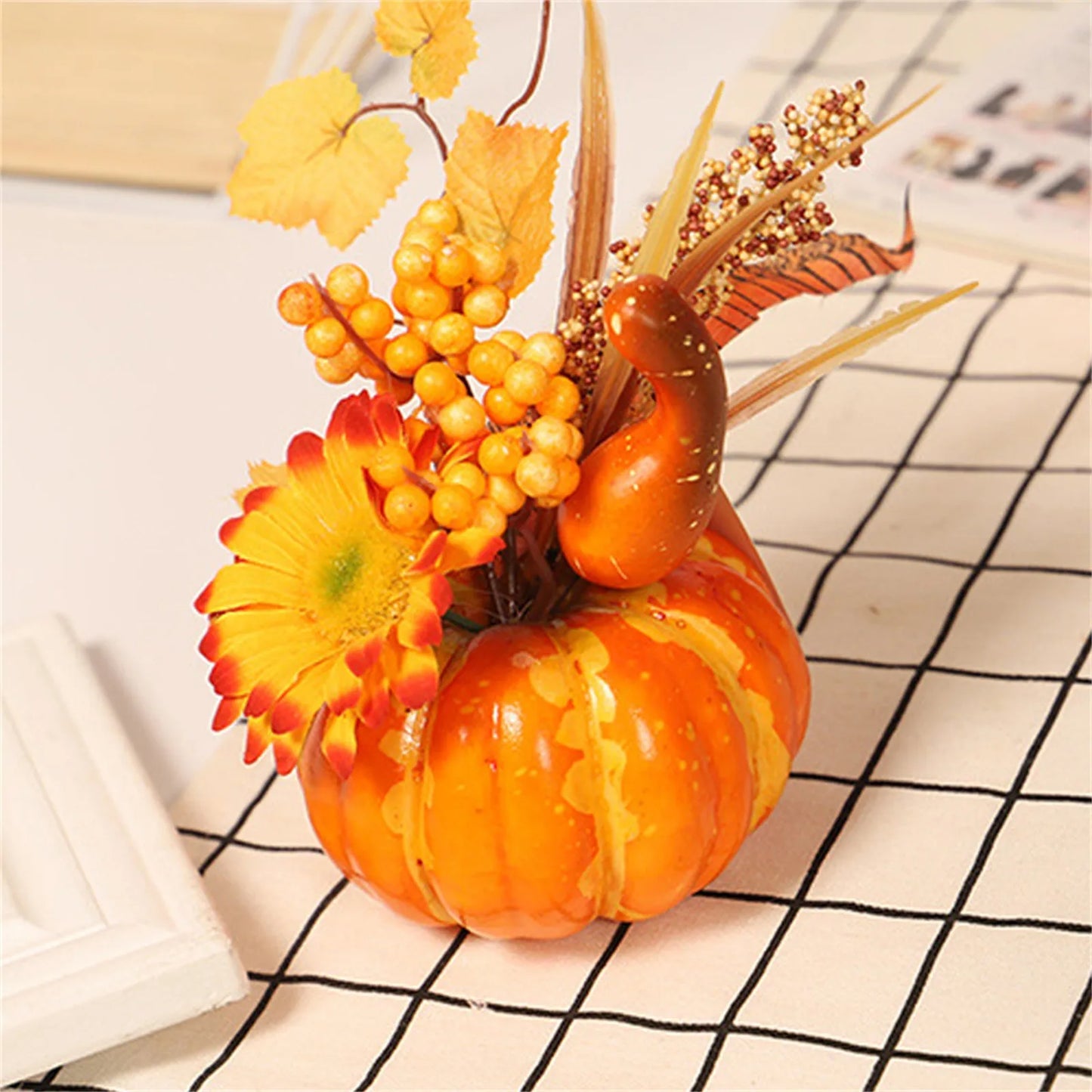 Decorative arrangement with a small pumpkin, flowers, and berries on a checkered tablecloth.