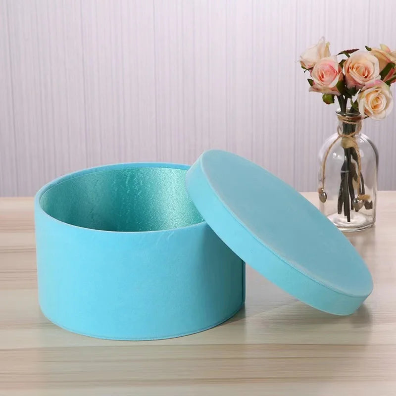 Light blue round storage box with lid on a wooden surface, with a vase of flowers in the background.