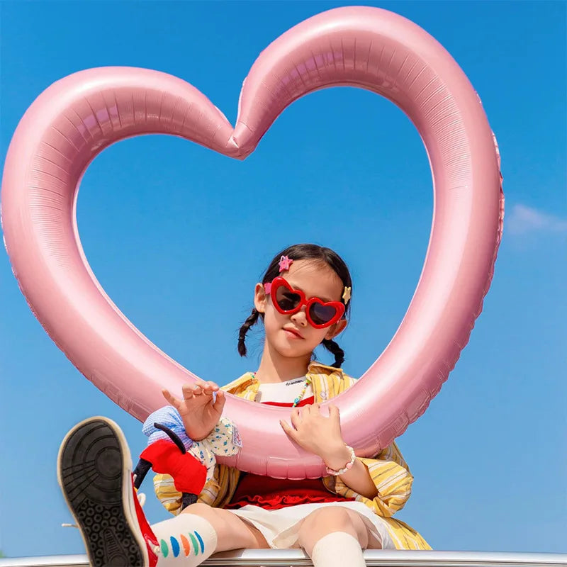 Child with heart-shaped sunglasses and pink heart-shaped object against a blue sky