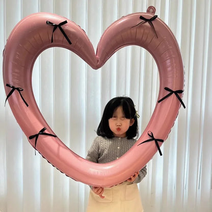 Child holding a large pink heart-shaped balloon with black ribbons against a white curtain background