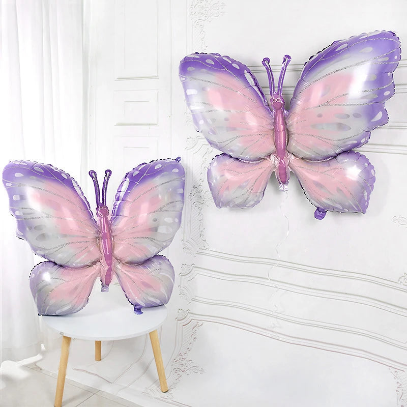 Two butterfly-shaped balloons in pink and purple on a white chair against a white wall.