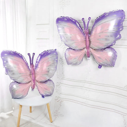 Two butterfly-shaped balloons in pink and purple on a white chair against a white wall.