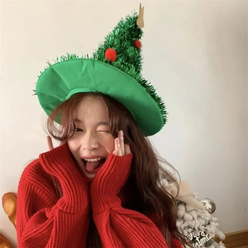 Person wearing a green Christmas tree hat and red sweater, posing playfully.