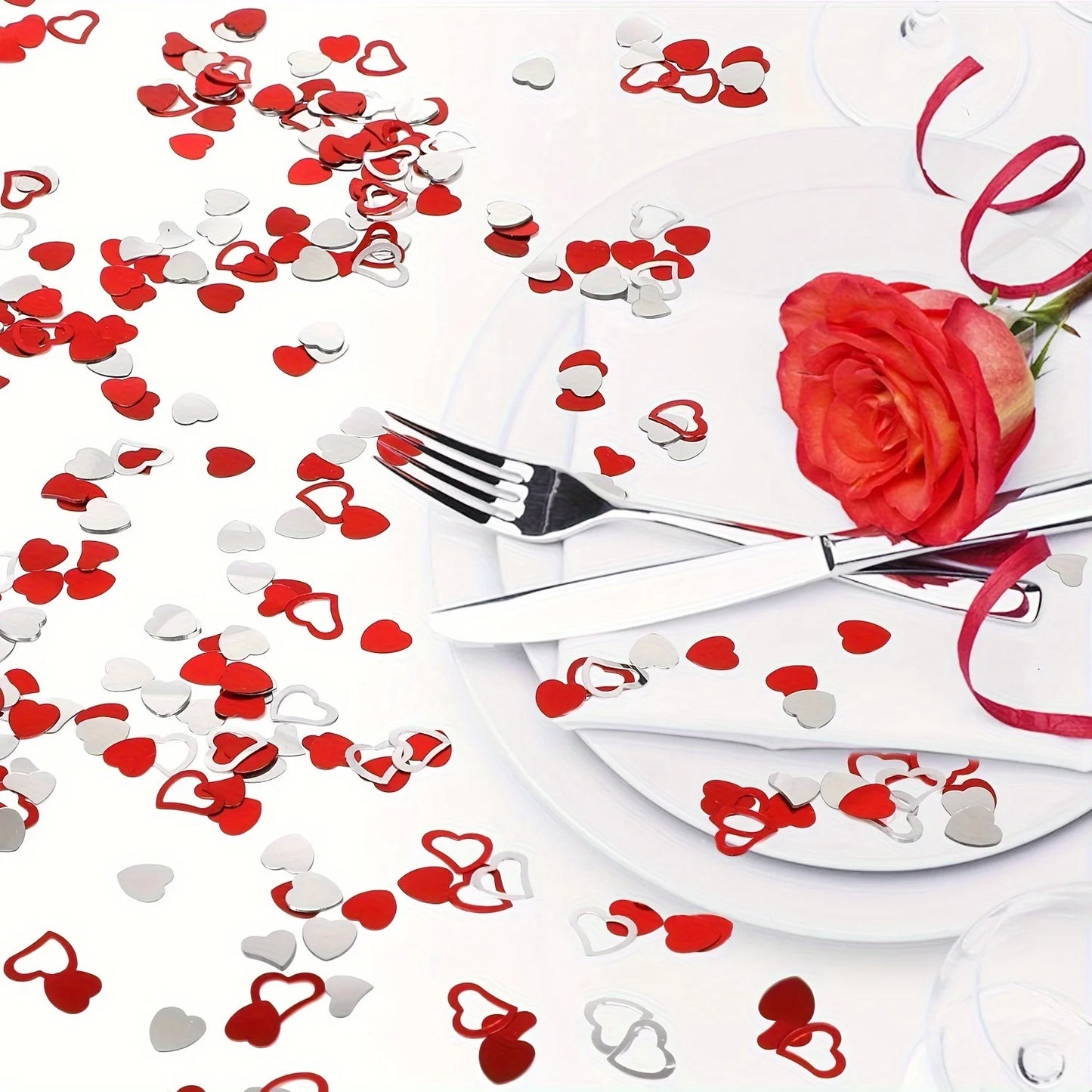 Dinner setting with red rose, silverware, and heart-shaped confetti on a white background