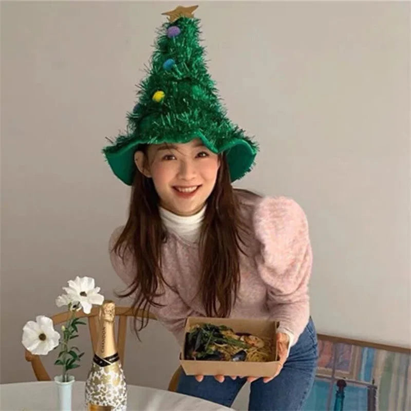 Person wearing a green Christmas tree hat, holding a box of food, with a neutral background.