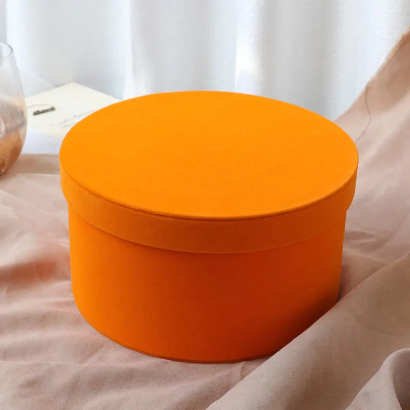 Orange round box on a light pink surface with a blurred background