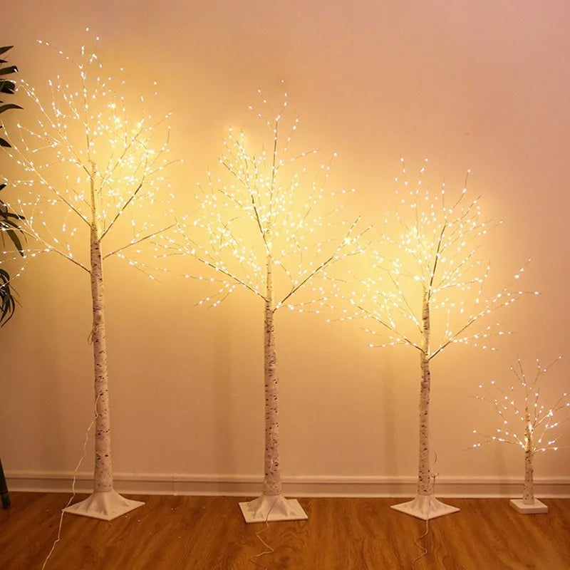 Set of four illuminated decorative trees on a wooden floor against a beige wall.