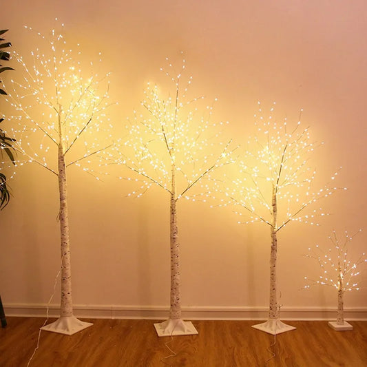 Set of four illuminated decorative trees on a wooden floor against a beige wall.