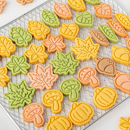Colorful leaf, mushroom, and pumpkin-shaped cookies on a cooling rack.