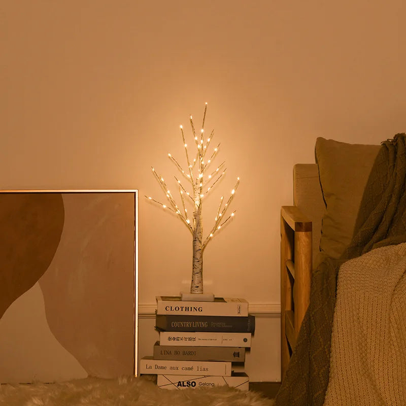 Decorative LED tree on a stack of books with a warm glow in a cozy room.