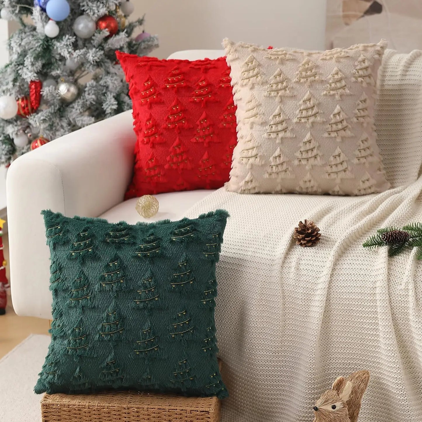 Decorative pillows with Christmas tree patterns on a couch next to a decorated Christmas tree.