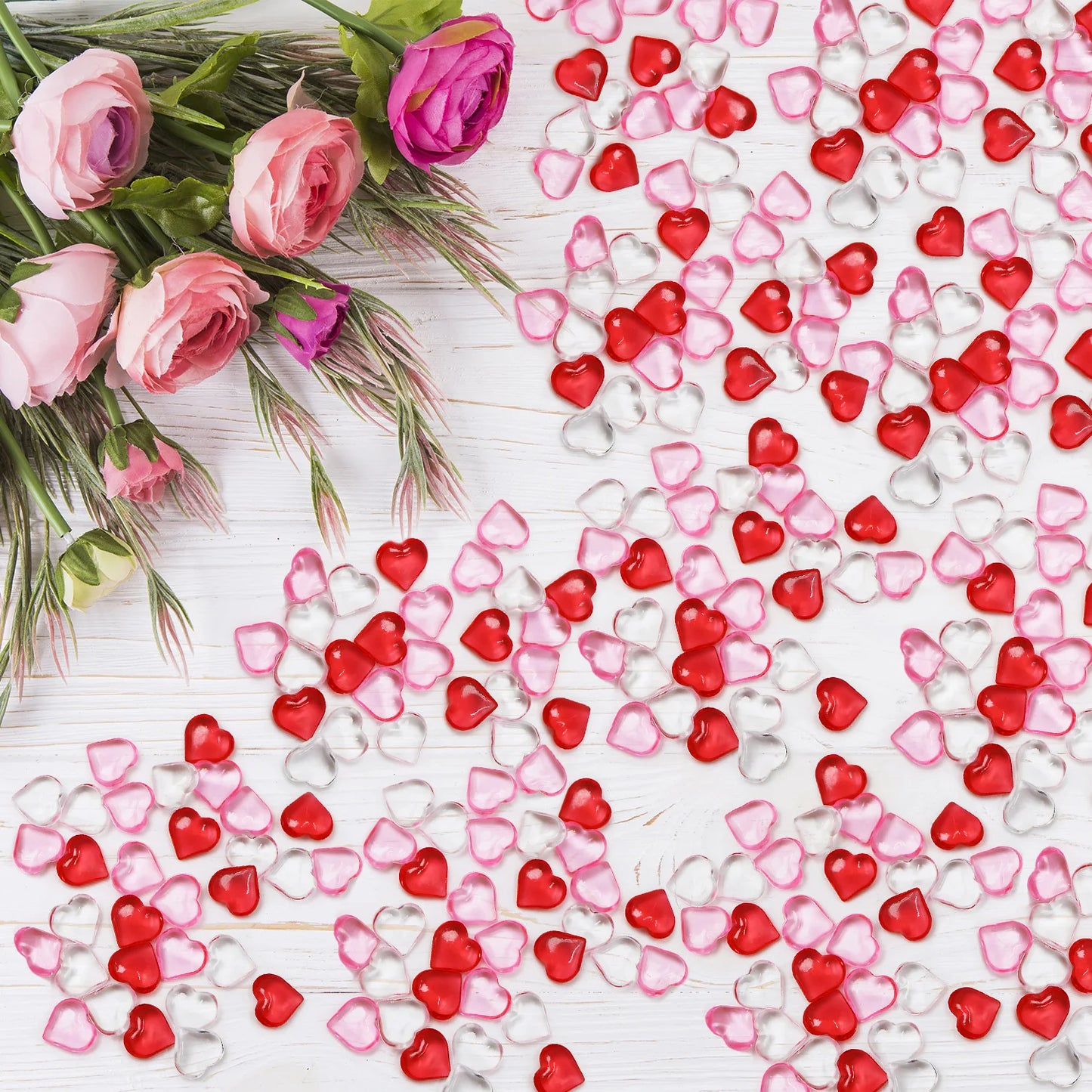 Heart-shaped confetti in red, pink, and clear on a white surface with pink roses.