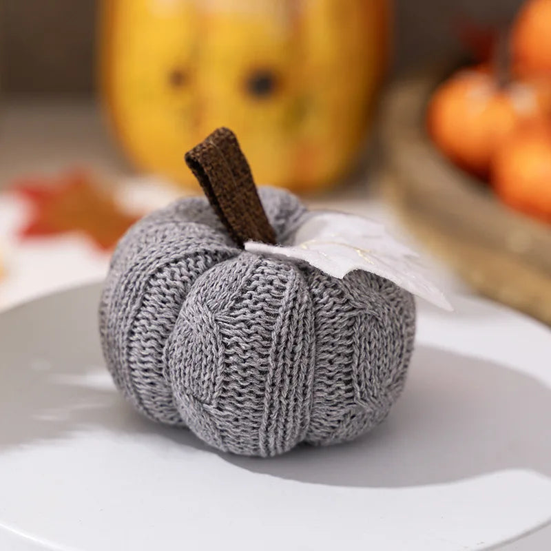 Knitted pumpkin decoration on a white plate with blurred pumpkins in the background