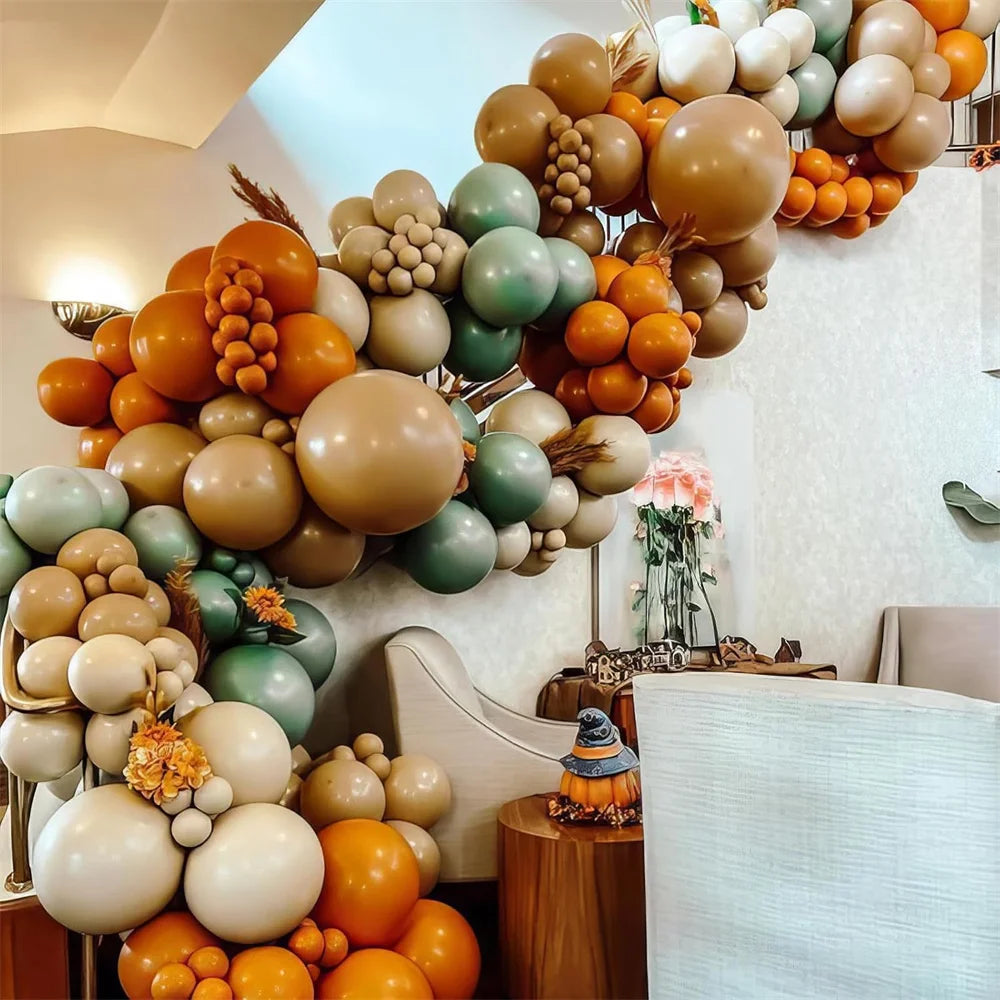 Balloon arch with orange, green, and beige balloons in a room setting.