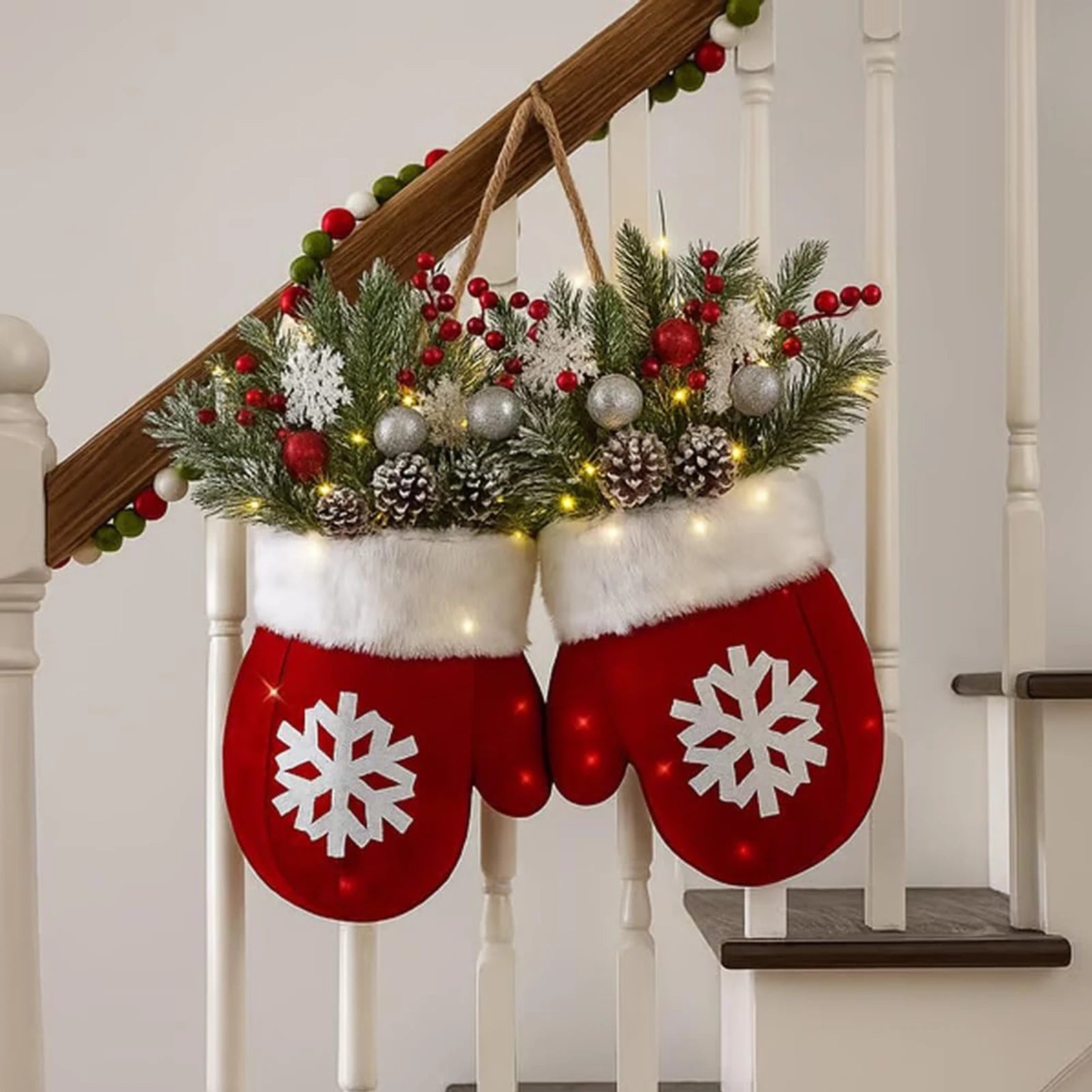 Red mitten-shaped stockings with snowflake designs hanging on a staircase decorated with greenery and lights.
