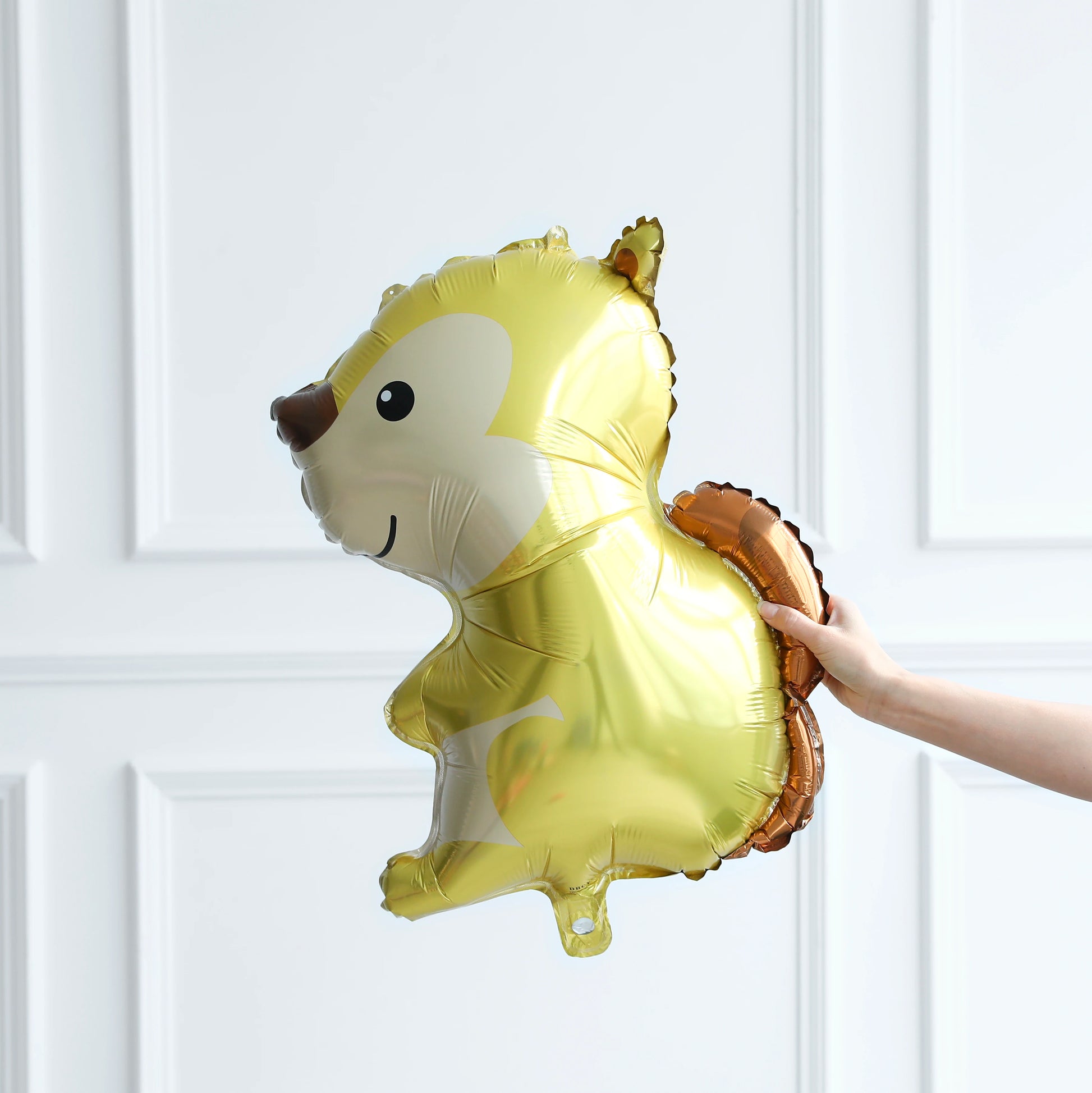 Gold squirrel-shaped balloon held against a white paneled wall