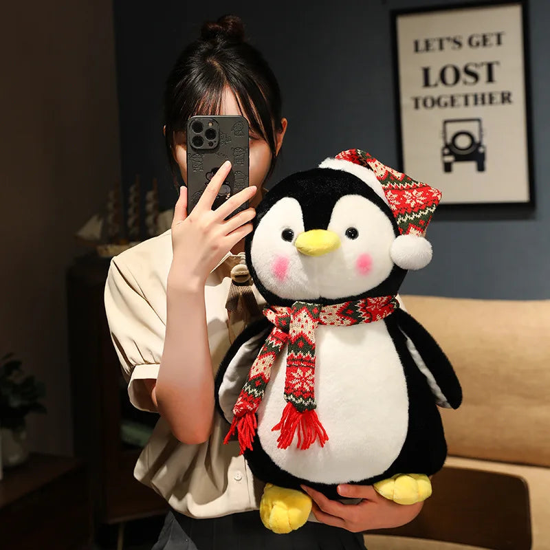 Person holding a plush penguin toy with a red scarf in a room.