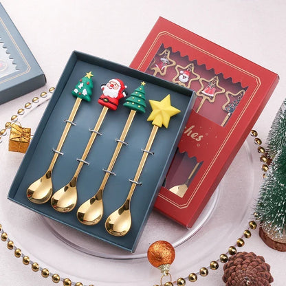 Set of four gold Christmas-themed spoons in a blue box with decorative items around.