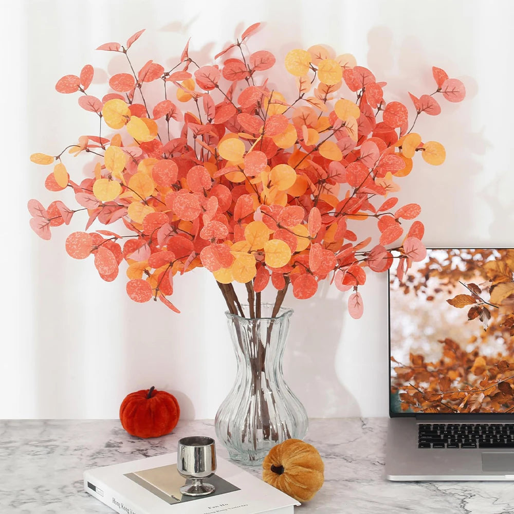 Decorative fall-themed arrangement with a vase of orange and yellow leaves on a marble surface.