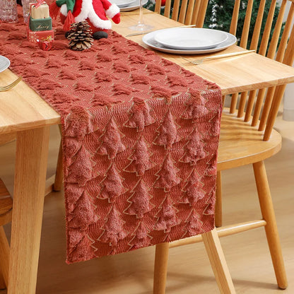 Dining table with a textured red table runner, plates, and glasses on a wooden table.